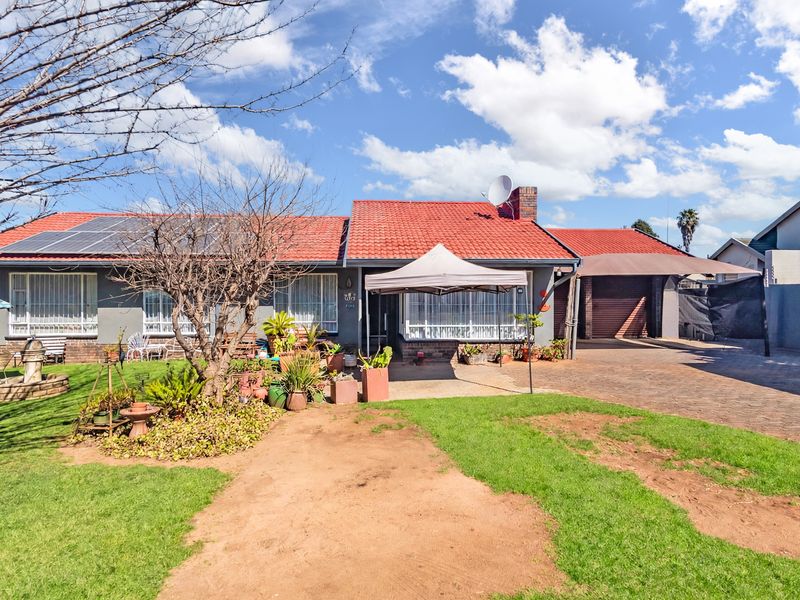 Front view of a single-story house featuring a tiled roof, solar panels, a paved driveway, and an attached carport.