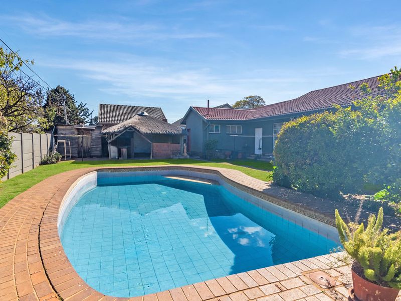 Rear garden featuring a swimming pool with brick coping, a thatched lapa, and a lawn area set against the rear building elevation.
