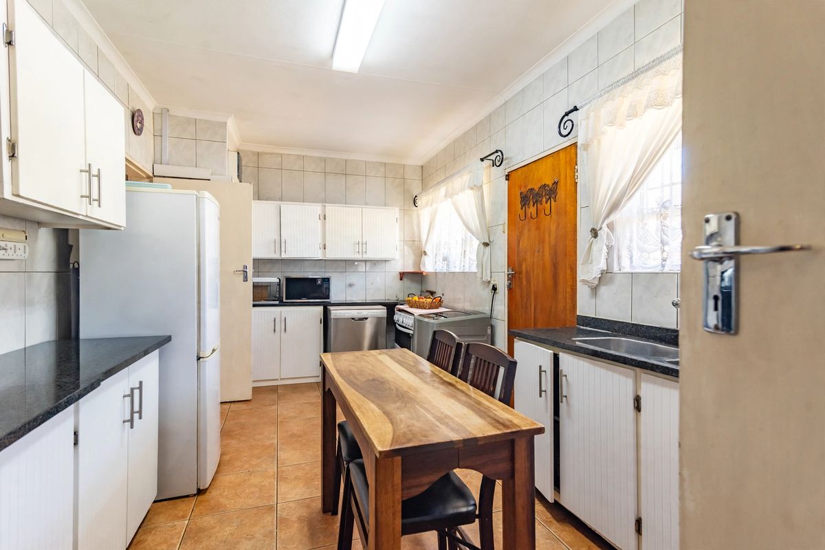 A functional kitchen featuring white cabinetry, dark laminate countertops, tiled backsplash, and ceramic floor tiles, offering a practical layout for daily meal preparation.