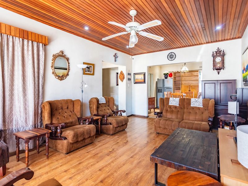 Spacious living room featuring a warm timber-slat ceiling, ceiling fan, and durable laminate flooring, offering a comfortable and traditional living space.