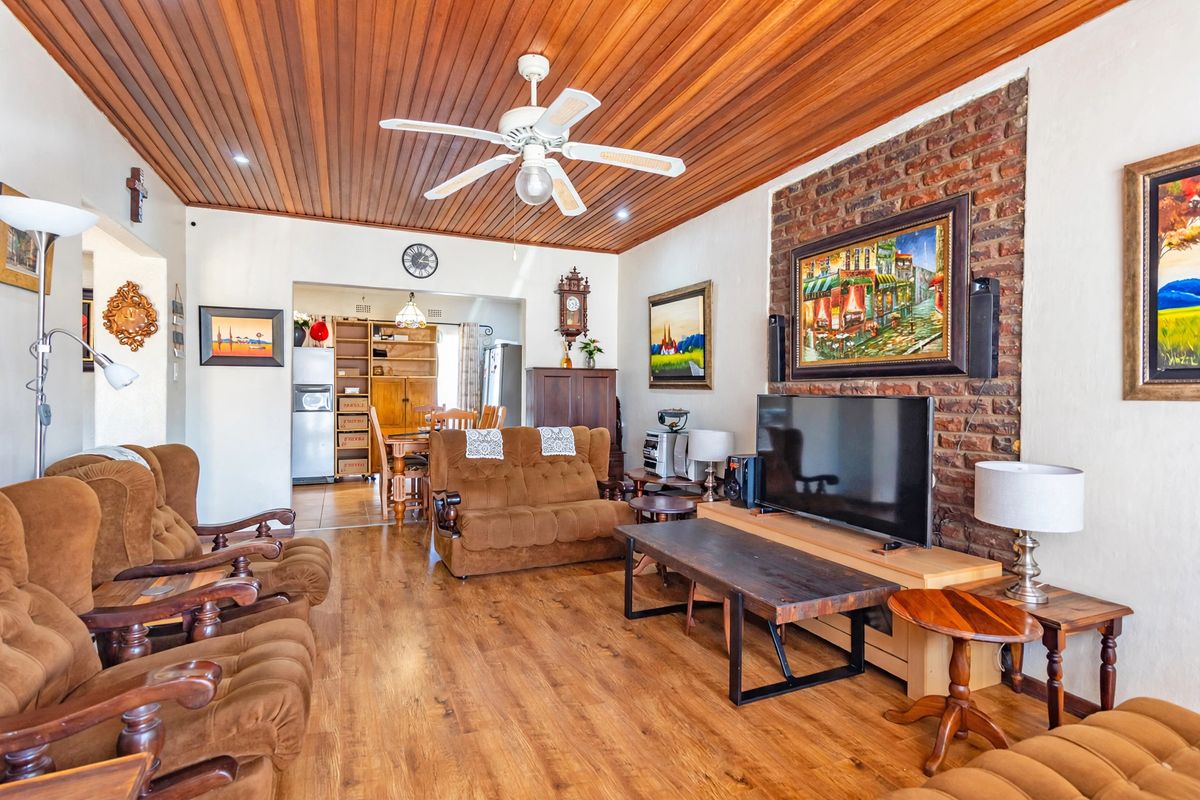 Spacious living room featuring a warm timber-paneled ceiling, ceiling fan, and a rustic exposed brick feature wall with laminate flooring throughout.
