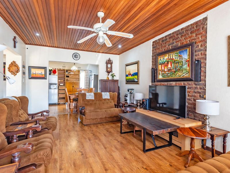 Spacious living room featuring a warm timber-paneled ceiling, ceiling fan, and a rustic exposed brick feature wall with laminate flooring throughout.