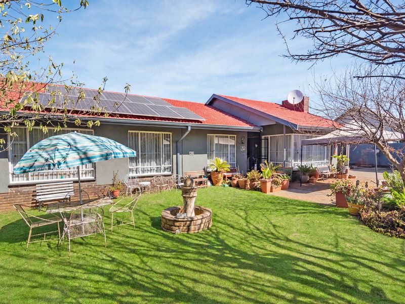 Rear view of the house featuring a well-maintained lawn, paved patio area, stone fountain, and roof-mounted solar panels.