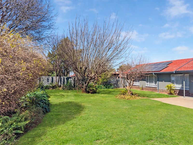A well-maintained rear garden featuring a lush lawn, mature trees, boundary wall, and a house exterior equipped with roof-mounted solar panels.