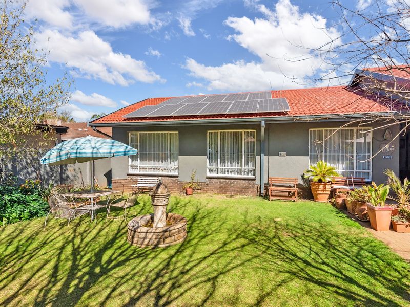 Rear view of the house featuring a well-maintained lawn, stone fountain, and roof-mounted solar panels.