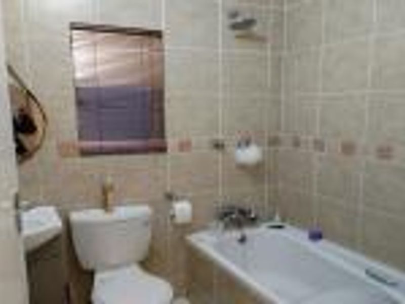 A functional bathroom featuring a bathtub with shower head, wall-mounted basin, and toilet, finished with neutral wall tiling.