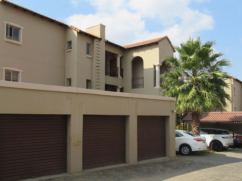 Exterior view of an apartment complex featuring multiple garage units, a paved driveway, and covered parking areas.