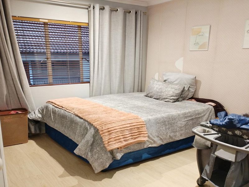A functional bedroom featuring light-toned laminate flooring, a built-in wardrobe, and window blinds, providing a neutral base for personalization.