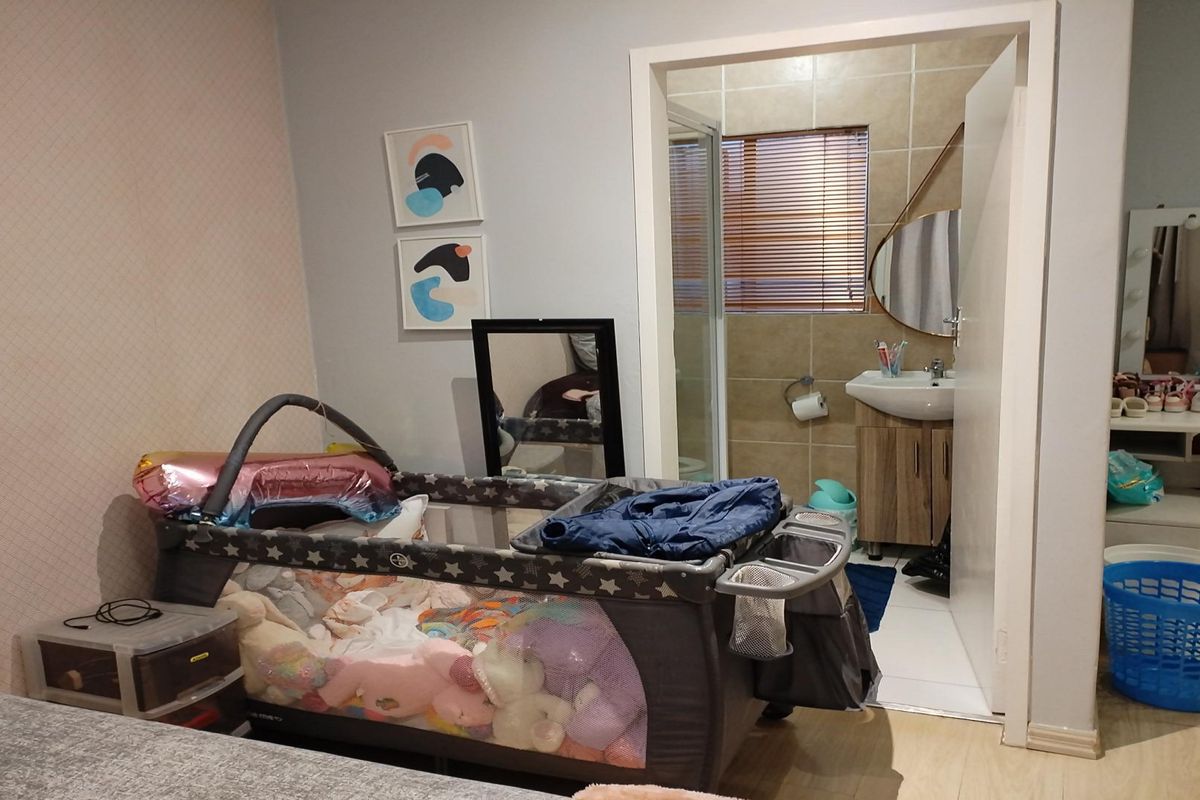 A bedroom featuring laminate flooring and an adjoining en-suite bathroom equipped with a vanity basin and shower enclosure.