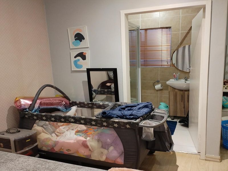 A bedroom featuring laminate flooring and an adjoining en-suite bathroom equipped with a vanity basin and shower enclosure.