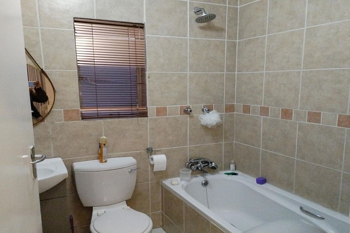 A functional bathroom featuring tiled walls, a combined bathtub and shower, a standard toilet, and a wall-mounted basin.