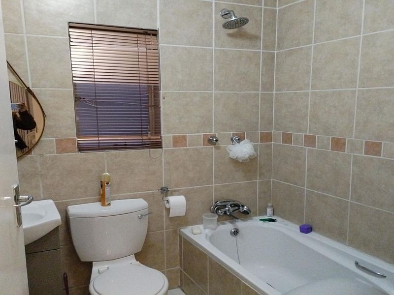 A functional bathroom featuring tiled walls, a combined bathtub and shower, a standard toilet, and a wall-mounted basin.