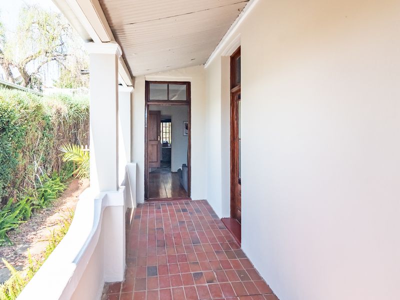 A covered outdoor patio featuring terracotta tile flooring, timber door frames, and a corrugated metal roof, providing access to the home's interior.