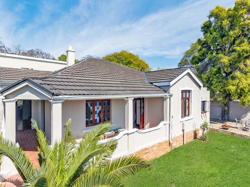 A well-maintained single-story house featuring a tiled roof, covered porch with concrete pillars, and stone base cladding, set within a landscaped garden.