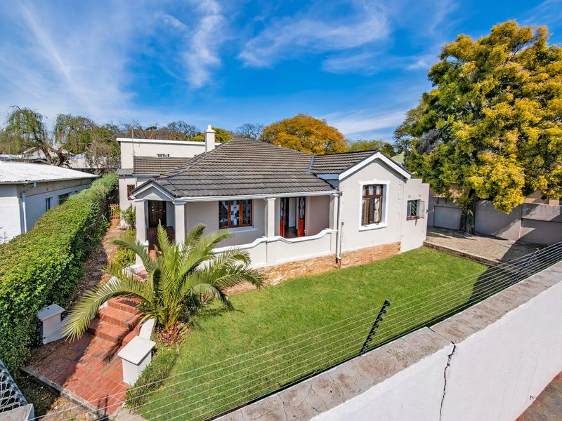 A well-maintained single-story house featuring a tiled roof, covered front porch, brick entrance steps, and a landscaped front garden with electric perimeter fencing.