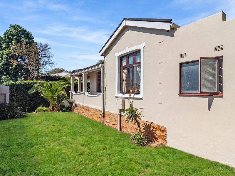 Rear view of the property featuring a lawn, stone-clad foundation, timber window frames, and a covered patio area.
