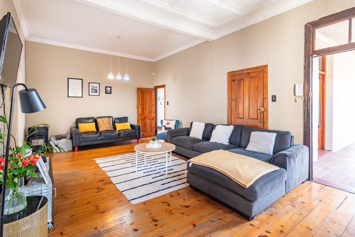 Spacious living room featuring original timber flooring, high ceilings with pressed metal detailing, and classic solid timber door frames.