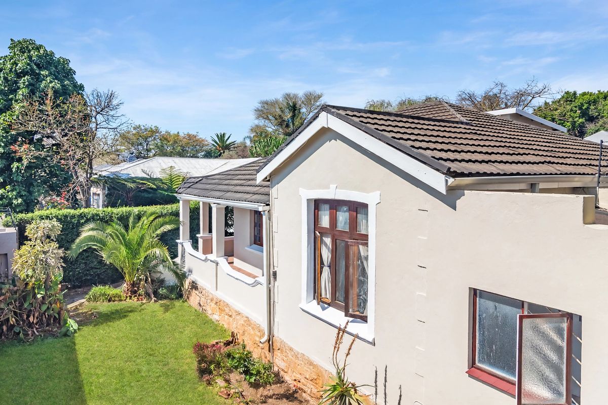 An elevated view of the rear exterior of the house, featuring a tiled roof, stone cladding, and a covered patio area overlooking the garden.