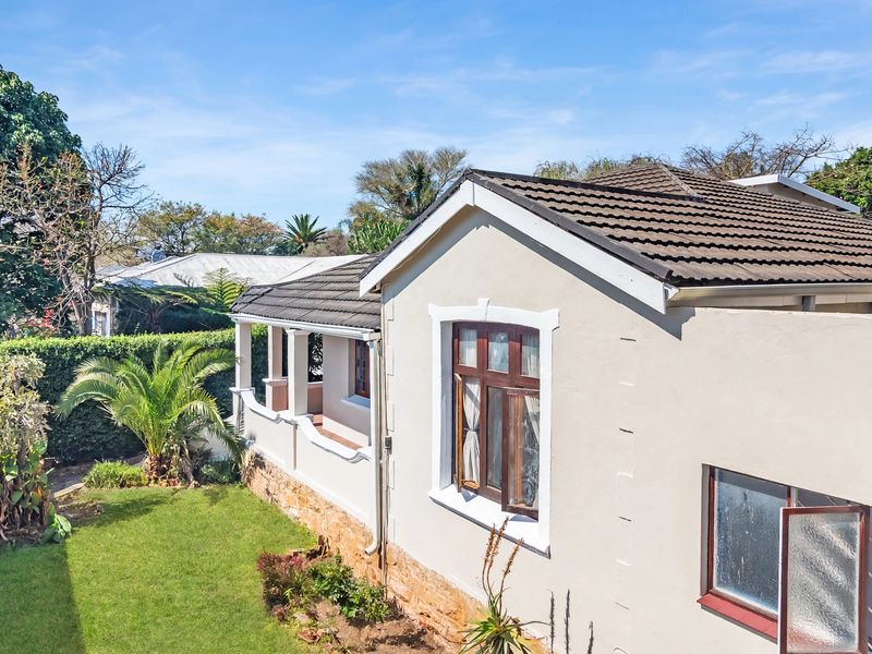 An elevated view of the rear exterior of the house, featuring a tiled roof, stone cladding, and a covered patio area overlooking the garden.