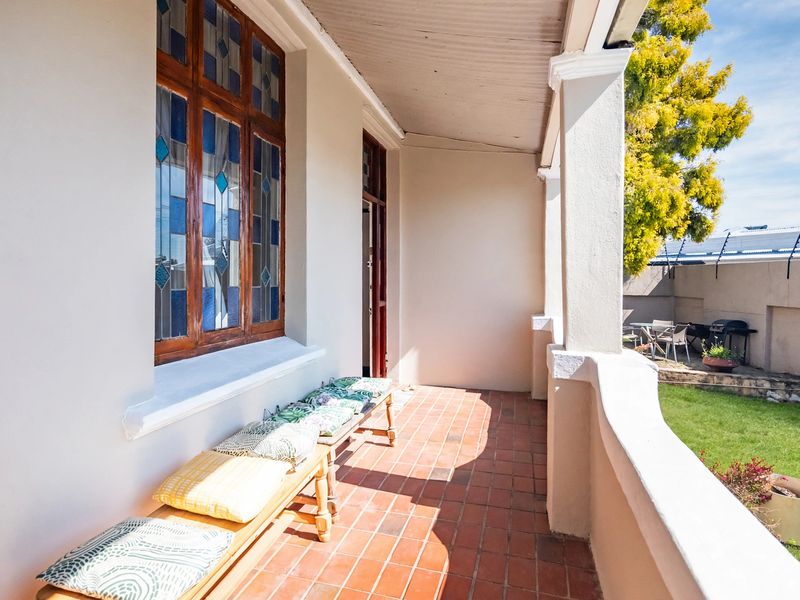 A covered veranda featuring terracotta tile flooring, classic concrete pillars, and a distinctive stained glass window overlooking a private garden area.