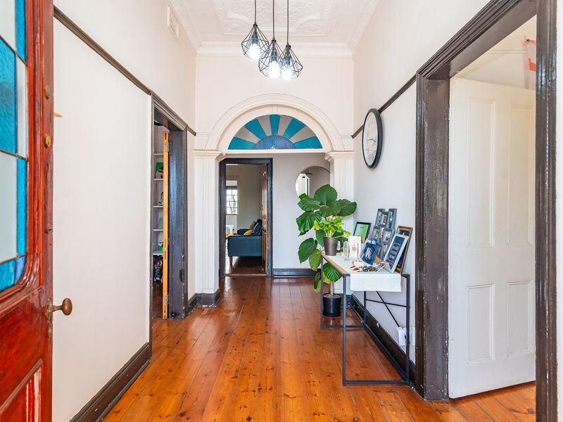 A bright, character-filled hallway featuring original timber flooring, decorative ceiling details, and a classic arched entryway with stained glass accents.
