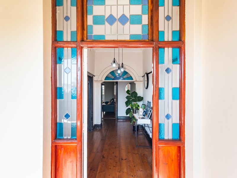 A welcoming hallway featuring original hardwood flooring, a decorative stained glass door frame, and an elegant architectural archway leading to the interior living spaces.