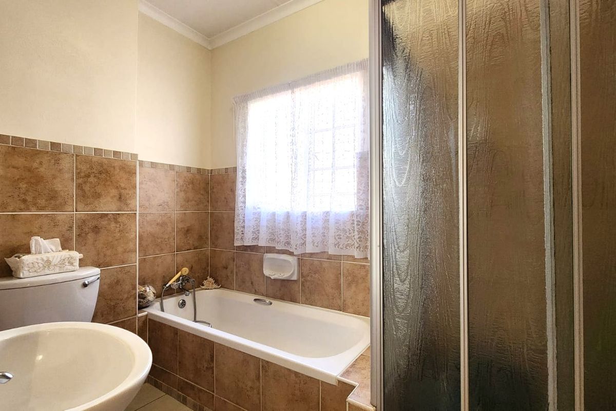 A functional bathroom featuring a bathtub, separate shower enclosure, and neutral brown wall tiling.