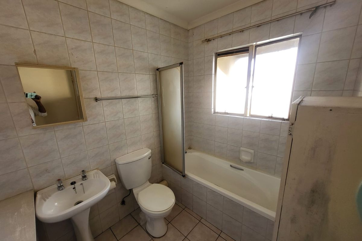 A dated bathroom featuring a pedestal basin, toilet, and a bathtub with a shower screen, finished with original wall and floor tiling.