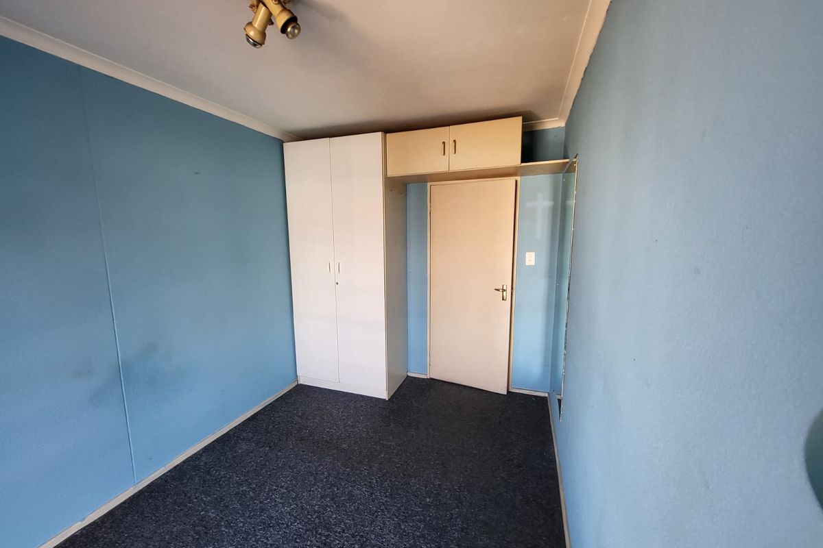 An empty bedroom featuring built-in wardrobe storage, overhead cupboards, and carpeted flooring, ready for a fresh update.