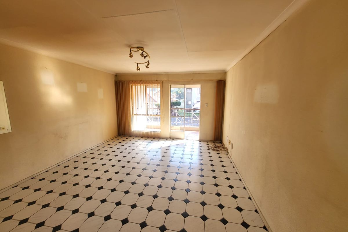 An empty living room featuring patterned tile flooring, a sliding glass door leading to a balcony, and vertical blinds.
