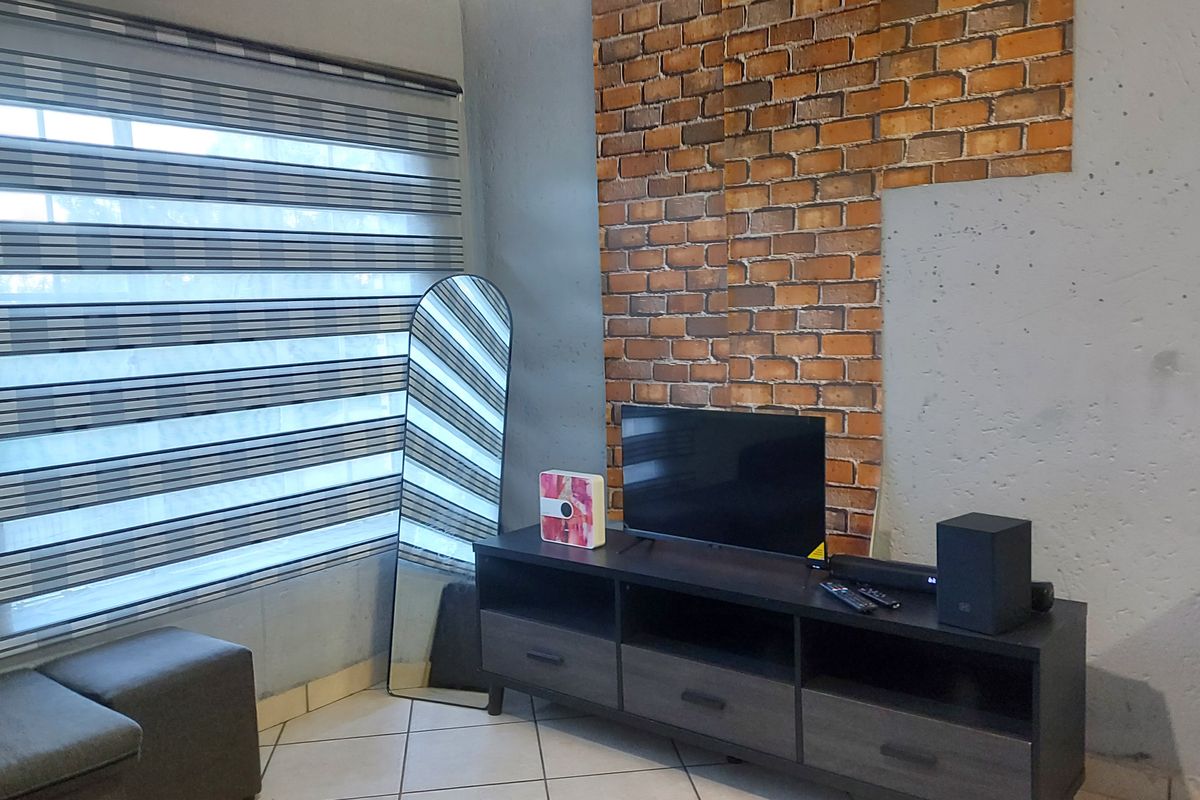 Living room area featuring an exposed brick accent wall, tiled flooring, and modern zebra blinds.