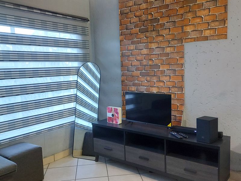 Living room area featuring an exposed brick accent wall, tiled flooring, and modern zebra blinds.