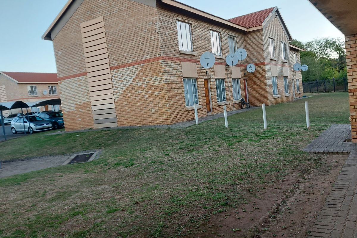 Exterior view of a face brick apartment complex featuring a shared lawn, paved walkways, and dedicated carport parking areas.