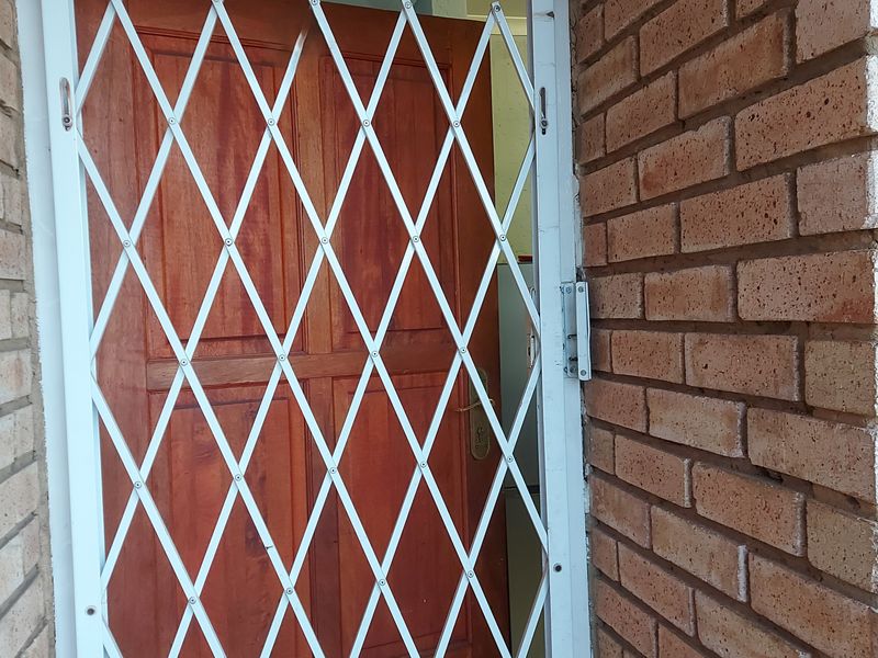 A secure entrance featuring a white metal security gate and a solid timber door set within a face brick exterior wall.