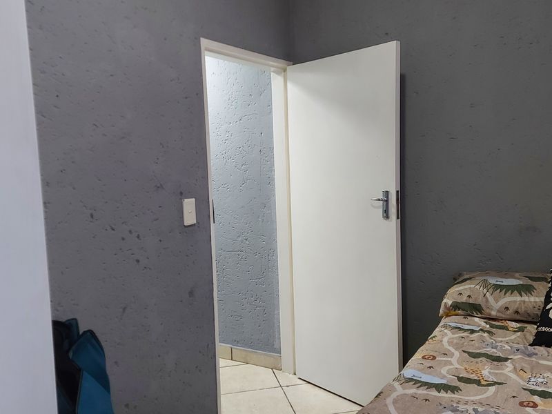 A bedroom featuring tiled flooring and a standard internal door, with grey textured walls showing signs of wear.