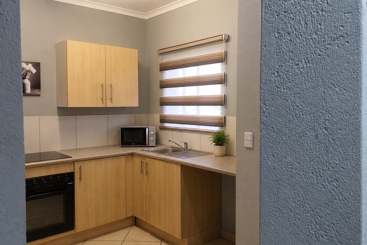 A compact, well-maintained kitchen featuring light wood-finish cabinetry, integrated oven and hob, and neutral tiled flooring with a functional layout.