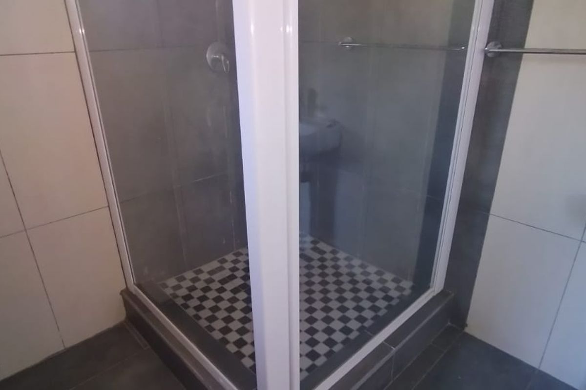A functional bathroom featuring a corner shower enclosure with a checkered floor, tiled walls, and a pedestal basin.