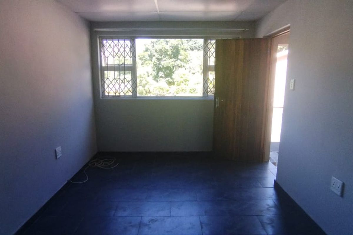 An empty bedroom featuring dark tiled flooring, a timber door, and a window fitted with a security gate.