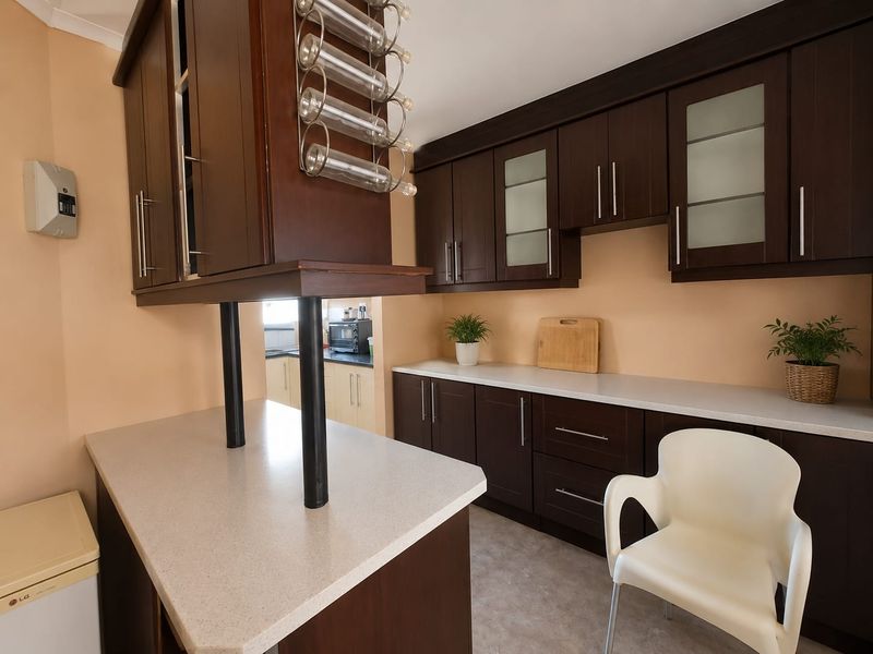 A functional kitchen featuring dark wood cabinetry, light-toned laminate countertops, and a breakfast bar with integrated wine storage.