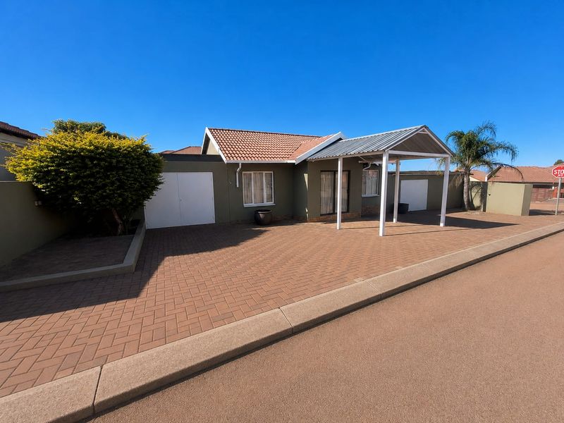 Front exterior view of a well-maintained house featuring a paved driveway, covered carport, and secure garage access.