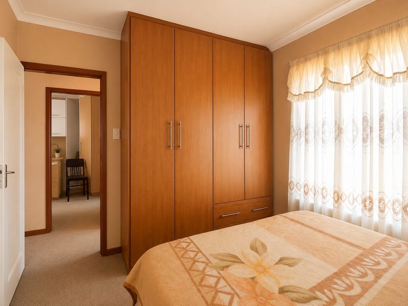 A bedroom featuring built-in wooden wardrobes, neutral carpet flooring, and a window with natural light.