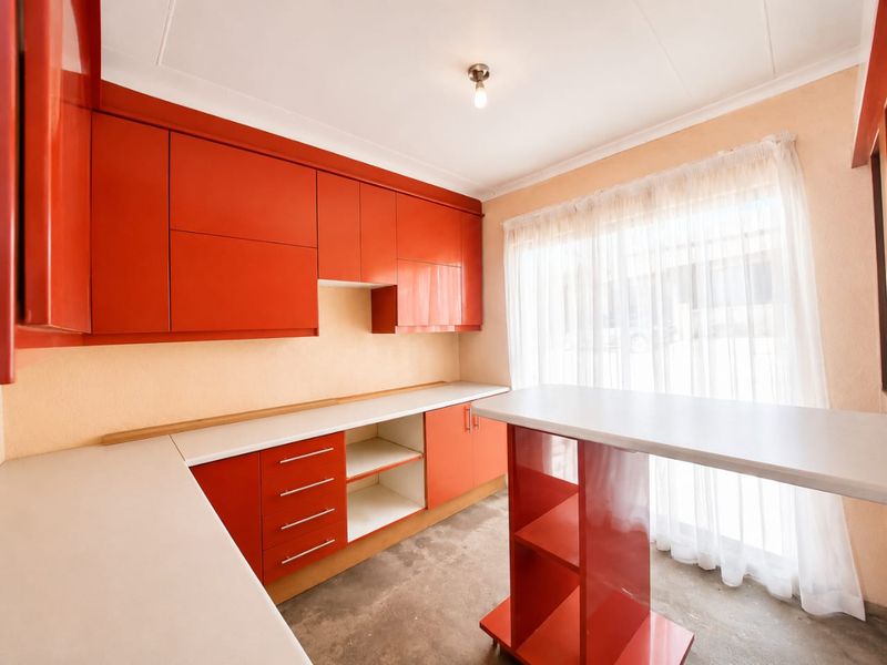 A functional kitchen space featuring vibrant red built-in cabinetry, white laminate countertops, and a matching breakfast bar island.