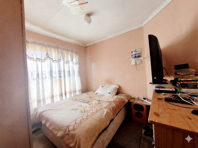 A compact bedroom featuring a window with curtains and a ceiling light fixture, requiring cosmetic updates and ceiling repairs.