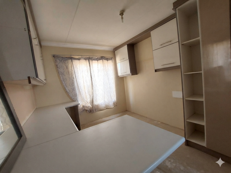 An empty kitchen space featuring built-in cabinetry, laminate countertops, and open shelving, requiring cosmetic updates to flooring and wall finishes.