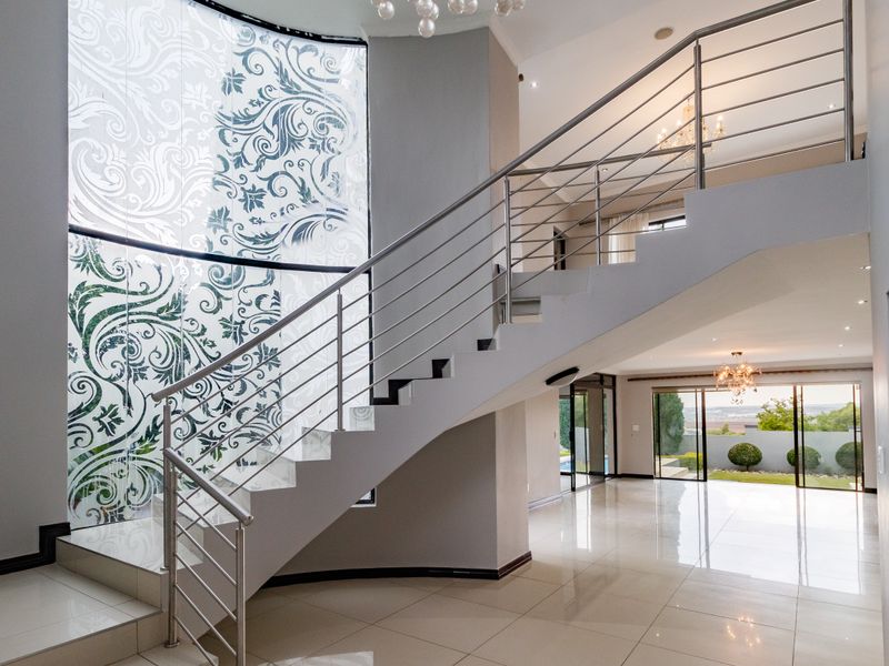 Spacious entrance hall featuring a modern staircase with stainless steel balustrades, large decorative window, and polished tiled flooring leading to an open living area.