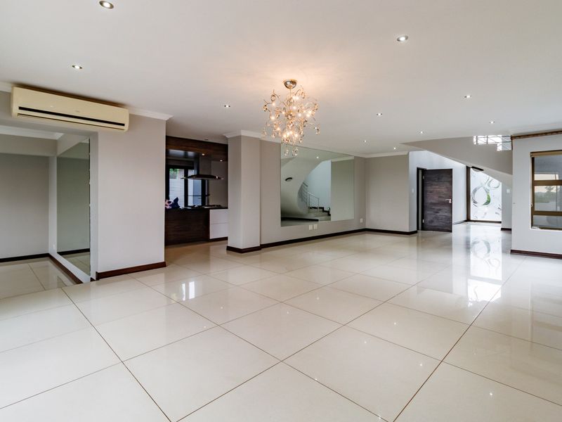 Spacious open-plan living area featuring polished porcelain floor tiles, recessed lighting, a wall-mounted air conditioner, and a feature staircase.