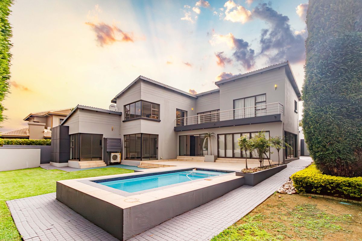 Rear view of a modern two-story house featuring a swimming pool, paved patio area, balcony, and well-maintained garden landscaping.