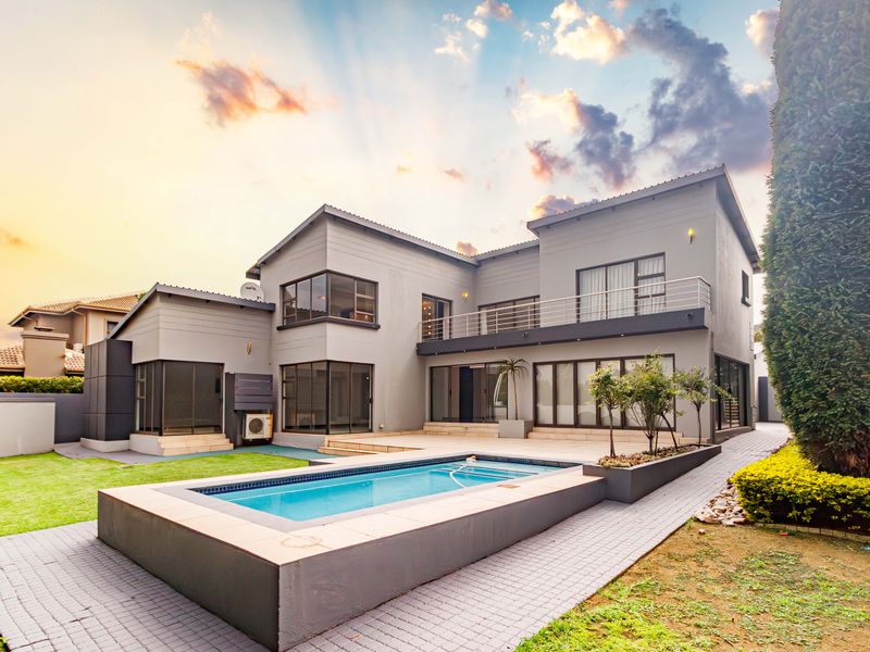 Rear view of a modern two-story house featuring a swimming pool, paved patio area, balcony, and well-maintained garden landscaping.