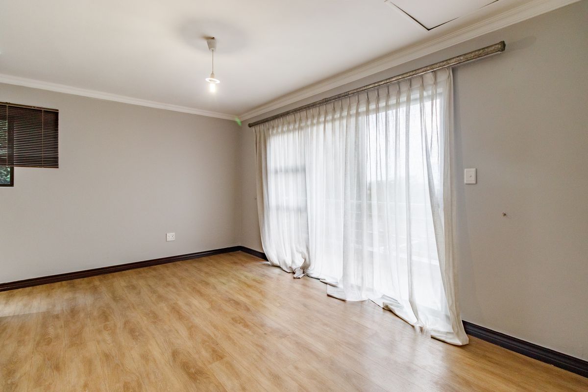 A bright, empty bedroom featuring light wood-look laminate flooring, neutral walls, and a large sliding glass door with sheer curtains leading to an outdoor area.