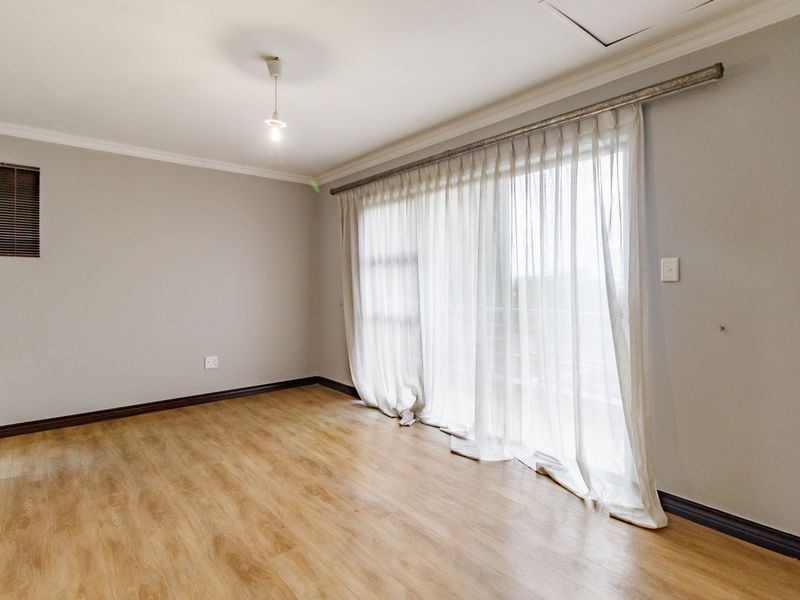 A bright, empty bedroom featuring light wood-look laminate flooring, neutral walls, and a large sliding glass door with sheer curtains leading to an outdoor area.